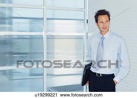 Businessman carrying laptop in office View Large Photo Image Stock Image - Businessman carrying laptop in office. Fotosearch