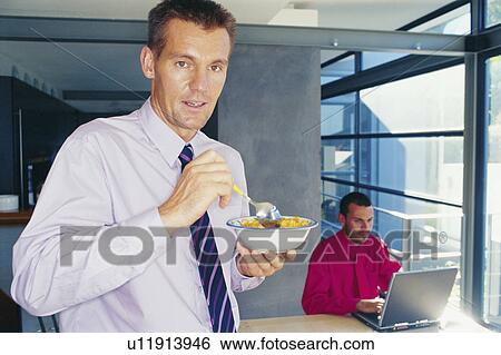 Stock Photograph - Businessman eating cereal in office. Fotosearch