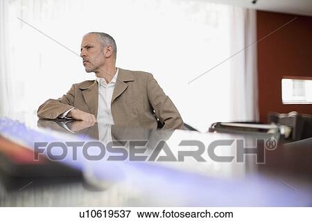 Businessman leaning on desk in office View Large Photo Image Stock Photo - Businessman leaning on desk in office. Fotosearch