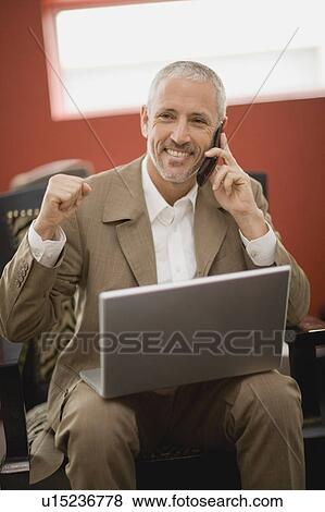 Stock Photo - Businessman on phone using laptop. Fotosearch
