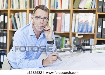Stock Image - Businessman reading blueprints in office. Fotosearch