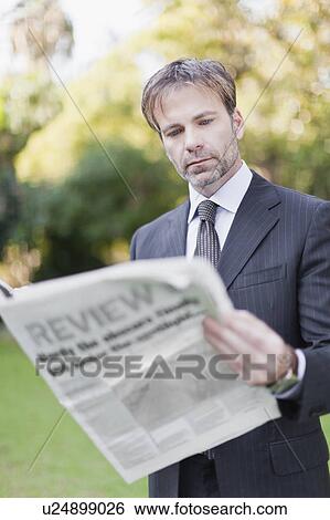 Stock Photograph - Businessman reading newspaper in park. Fotosearch
