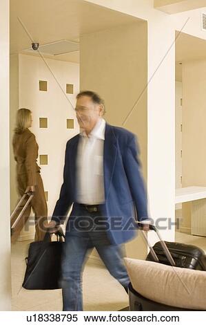 Stock Photography - Businessman rolling luggage in walkway. Fotosearch