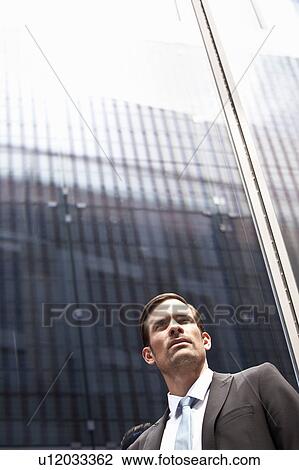 Stock Image - Businessman standing next to high rise. Fotosearch