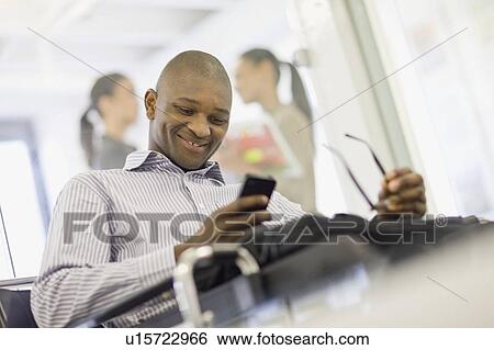 Stock Photograph - Businessman using cell phone in office. Fotosearch