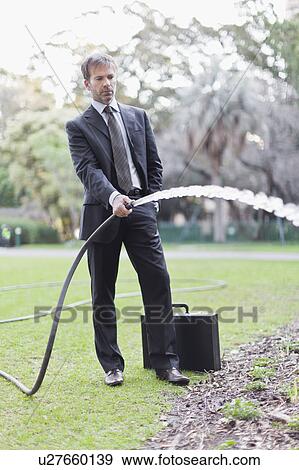 Businessman watering plans in park View Large Photo Image Stock Photo - Businessman watering plans in park. Fotosearch