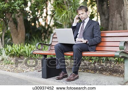 Stock Image - Businessman working on laptop in park. Fotosearch