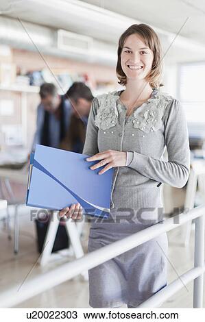 Stock Image - Businesswoman carrying folder in office. Fotosearch