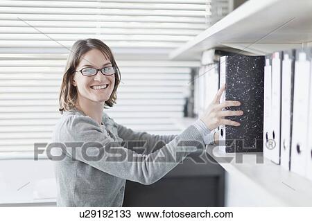 Stock Image - Businesswoman holding binder in office. Fotosearch