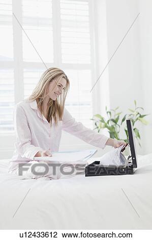 Stock Image - Businesswoman with briefcase on bed. Fotosearch