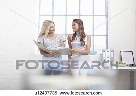 Businesswomen reading binder together View Large Photo Image Stock Photography - Businesswomen reading binder together. Fotosearch
