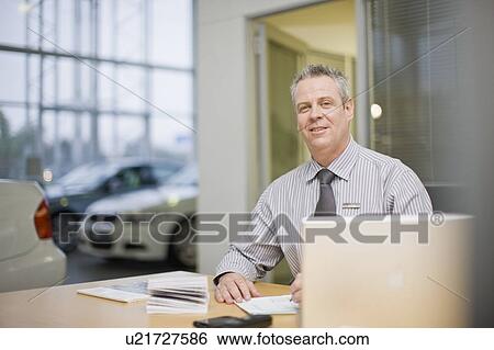 Car salesman sitting at desk in showroom View Large Photo Image Stock Photograph - Car salesman sitting at desk in showroom. Fotosearch