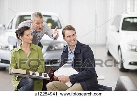 Stock Image - Car salesman talking with couple. Fotosearch