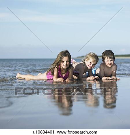 Stock Image - Children playing in waves on beach. Fotosearch