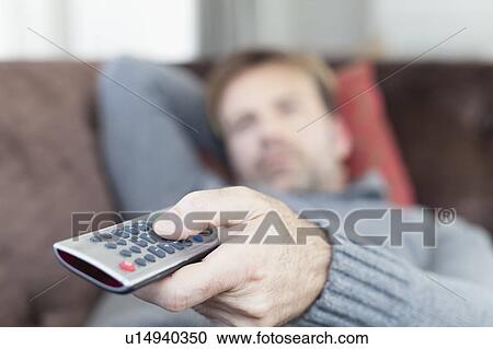 Stock Image - Close up of man using remote control. Fotosearch
