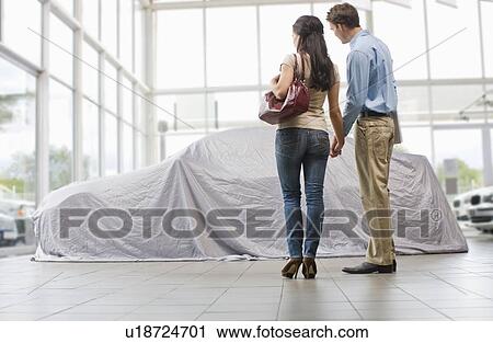 Stock Image - Couple admiring new car under cloth. Fotosearch