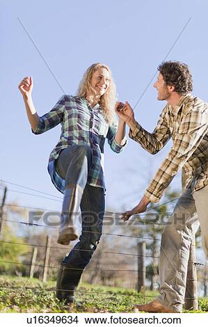 Picture - Couple climbing over wire fence outdoors. Fotosearch