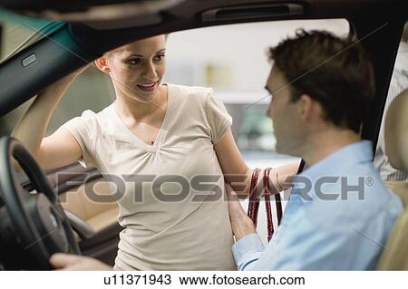 Stock Image - Couple examining car in showroom. Fotosearch