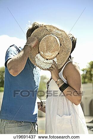 Stock Photo - Couple kissing behind sunhat in park. Fotosearch