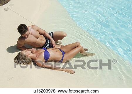 Stock Photo - Couple relaxing by swimming pool. Fotosearch