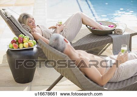 Couple relaxing in lawn chairs by pool View Large Photo Image Stock Image - Couple relaxing in lawn chairs by pool. Fotosearch