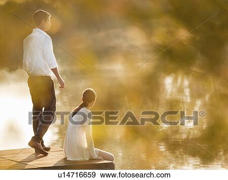 Stock Photo - Couple relaxing on dock of lake. Fotosearch