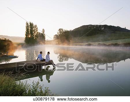 Stock Photo - Couple relaxing on dock of lake. Fotosearch