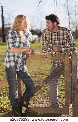 Stock Image - Couple talking on wooden fence outdoors. Fotosearch