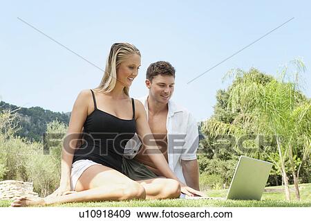 Stock Photo - Couple using laptop in grass together. Fotosearch