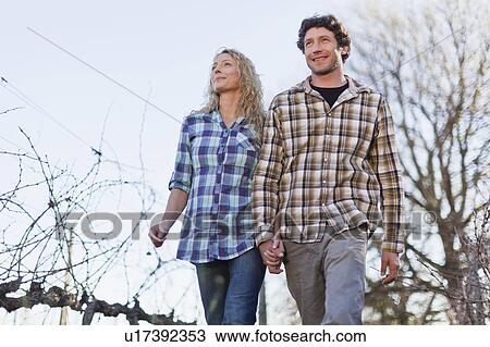 Stock Image - Couple walking hand-in-hand outdoors. Fotosearch