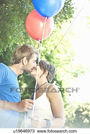 Couple with balloons kissing in park View Large Photo Image Stock Image - Couple with balloons kissing in park. Fotosearch