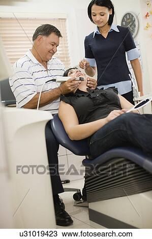 Stock Image - Dentist and assistant working on woman . Fotosearch
