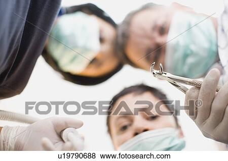 Dentists with tool peering over patient View Large Photo Image Stock Photo - Dentists with tool peering over patient. Fotosearch