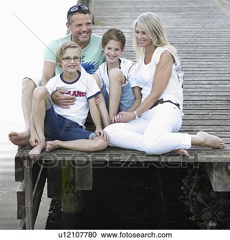 Stock Image - Family sitting together on dock. Fotosearch