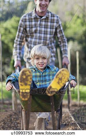 Stock Image - Father pushing son in wheelbarrow. Fotosearch