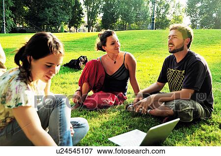 Stock Photo - Friends using laptop in grass in park. Fotosearch