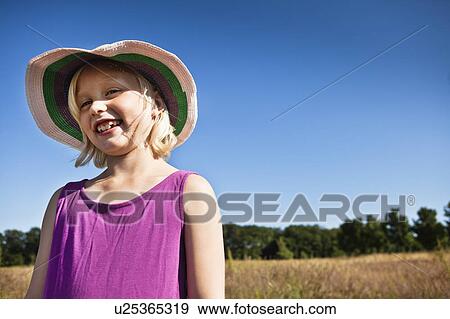 Stock Photo - Girl in sunhat smiling in field. Fotosearch