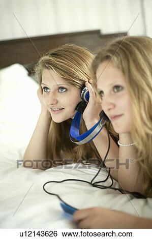 Girls listening to headphones on bed View Large Photo Image Stock Photograph - Girls listening to headphones on bed. Fotosearch