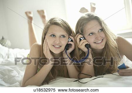 Girls listening to headphones on bed View Large Photo Image Stock Photography - Girls listening to headphones on bed. Fotosearch