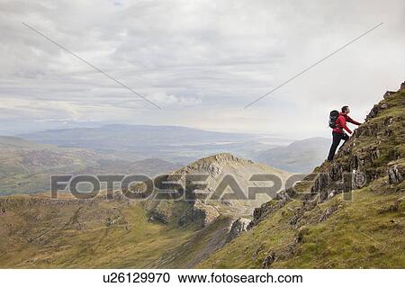Stock Image - Hiker climbing rocky mountainside. Fotosearch