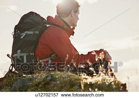 Stock Photo - Hiker sitting on grassy rock. Fotosearch