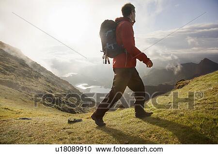 Stock Image - Hiker walking on grassy mountaintop. Fotosearch
