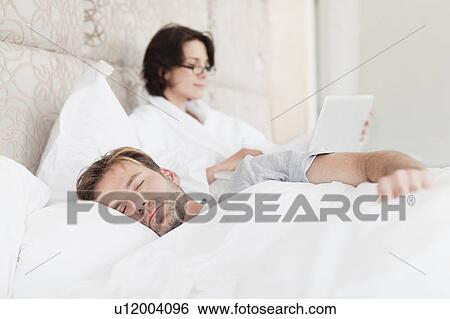 Stock Photograph - Man asleep next to working girlfriend. Fotosearch