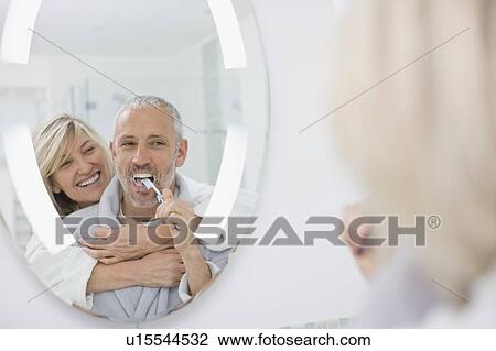 Stock Image - Man brushing his teeth with wife. Fotosearch