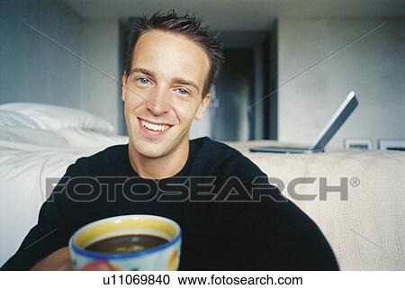 Stock Image - Man drinking cup of coffee in bedroom. Fotosearch