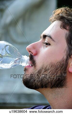 Picture - Man drinking from water bottle outdoors. Fotosearch