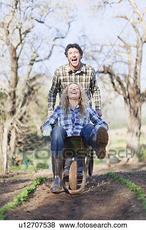 Stock Photo - Man pushing girlfriend in wheelbarrow. Fotosearch