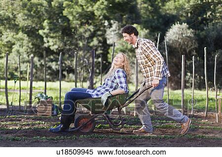 Stock Photography - Man pushing girlfriend in wheelbarrow. Fotosearch
