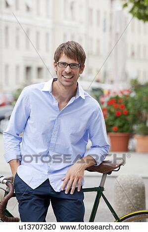Stock Image - Man standing with bike on city street. Fotosearch