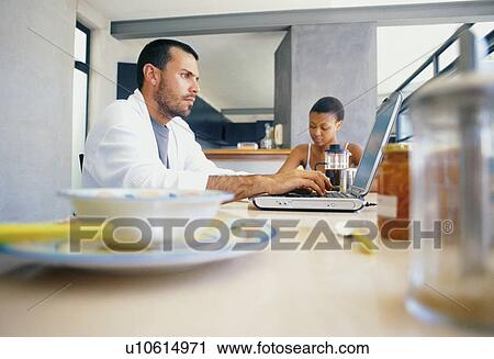 Stock Image - Man using laptop at breakfast table. Fotosearch